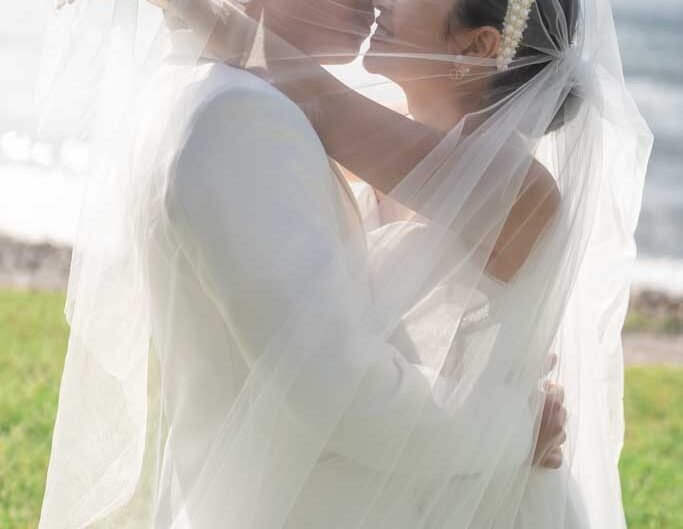 The bride and groom share a delicate kiss under the bridal veil, with Lake Como’s serene waters behind them.