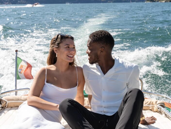A couple enjoying a boat ride on a sunny day, with clear blue waters and mountains in the background, Lake Como Proposal