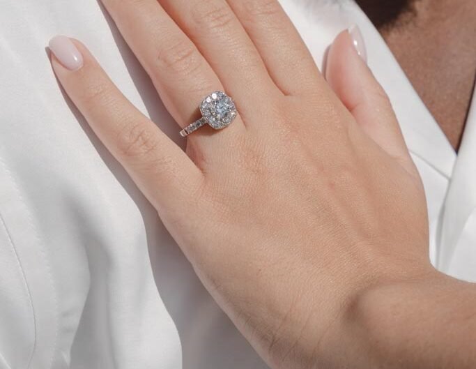 A hand with a freshly manicured nail polish displaying an engagement ring, resting on a white shirt