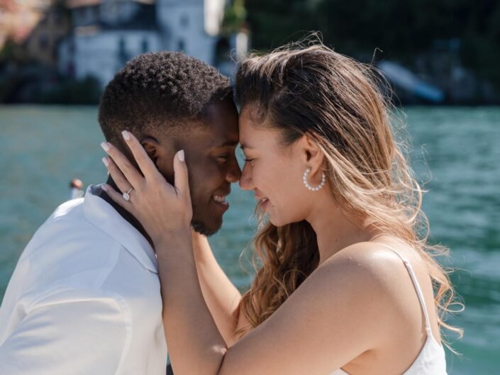 Close-up of a couple about to kiss, with the woman placing her hand on the man's cheek, showcasing an engagement ring, on Lake Como