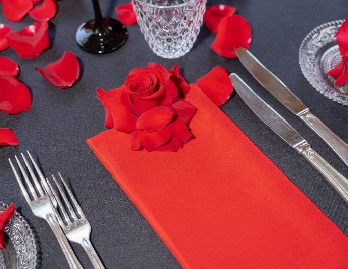 Elegant table setting with a red napkin, rose, and scattered petals for a romantic occasion