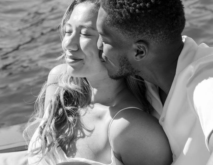 A black-and-white close-up of a couple in a tender moment on a boat, with the man kissing the woman on the cheek